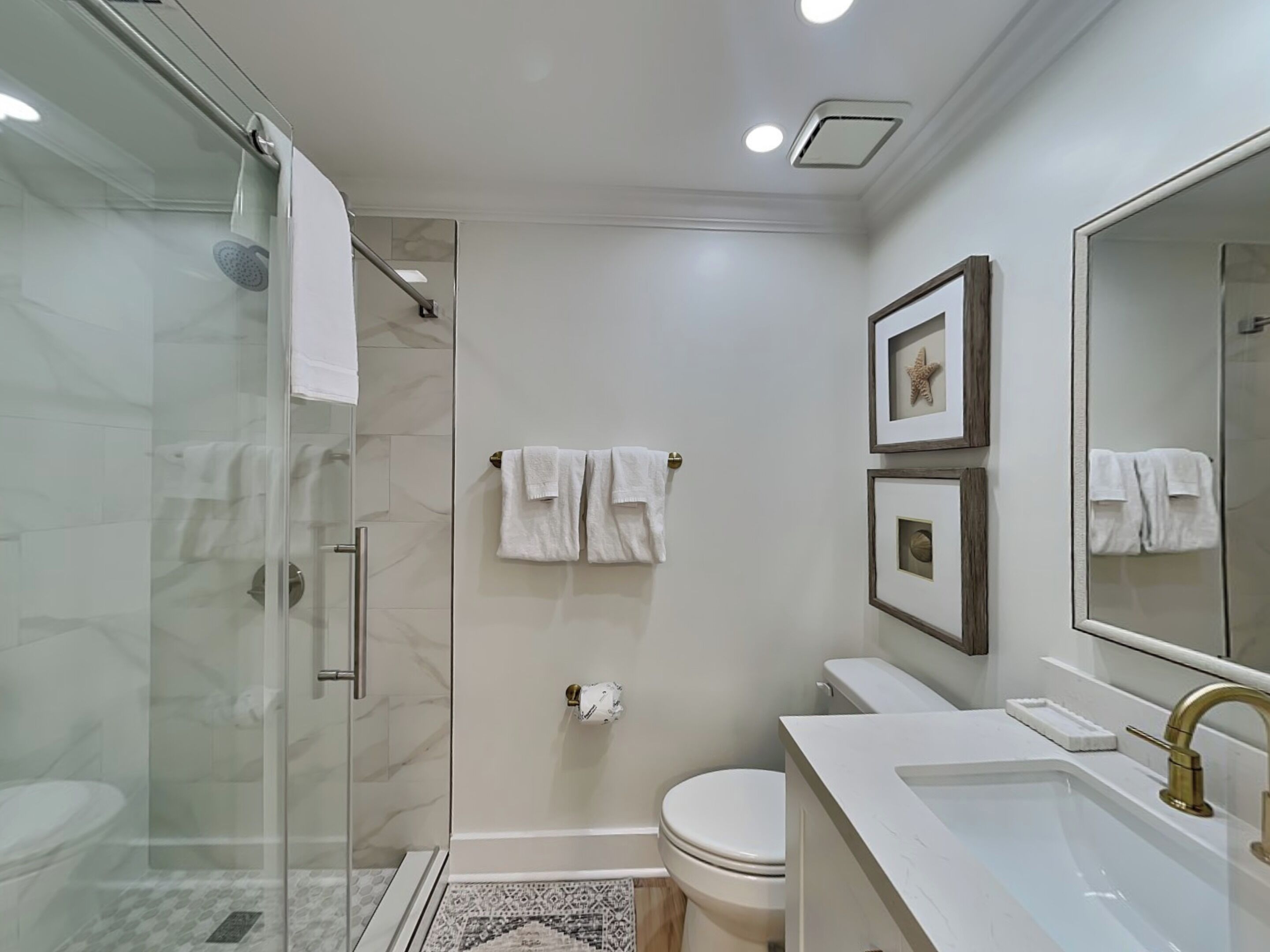 A modern bathroom with a glass shower enclosure, a toilet, and a sink with a gold faucet.