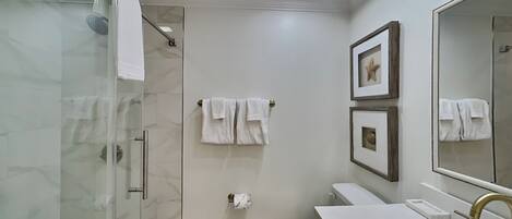 A modern bathroom with a glass shower enclosure, a toilet, and a sink with a gold faucet.