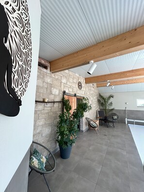 Un patio interno con parete in pietra, travi in legno, una pianta sospesa e arredi.