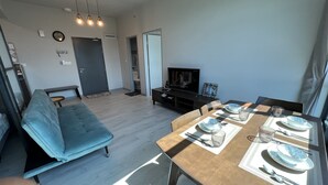 A modern living room with a sofa, dining table set with plates and glasses, a television, and a ceiling fan.