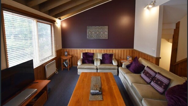 A cozy living room with a wooden ceiling, a sofa set, a coffee table, and a television.