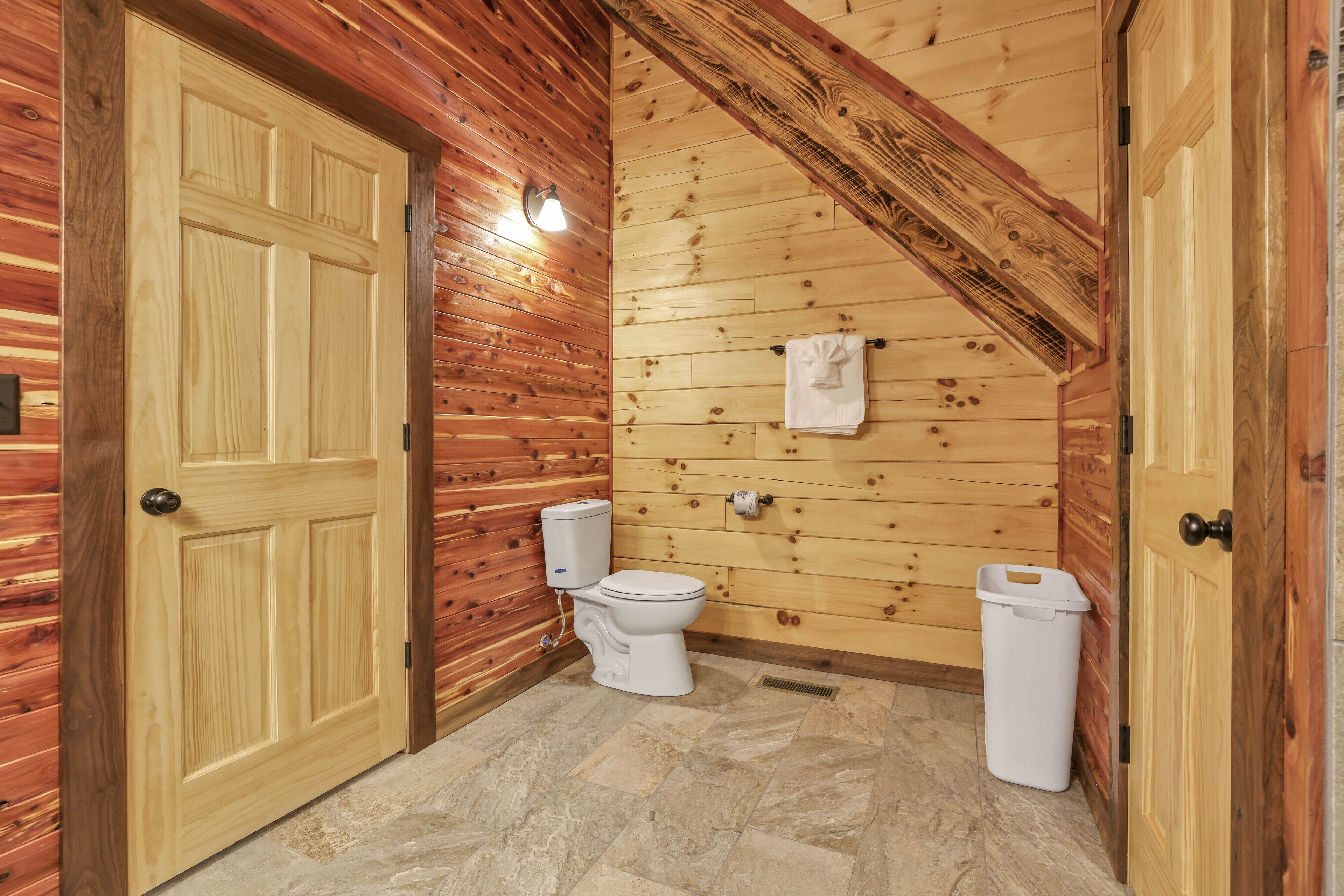 A wooden-paneled bathroom with a toilet, a trash can, and a towel hanging on the wall.