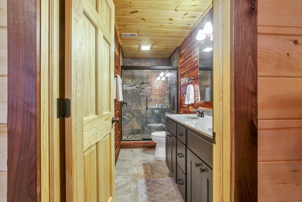 Une salle de bain rustique, aménagée dans une cabane en bois, avec douche, toilettes et lavabo.
