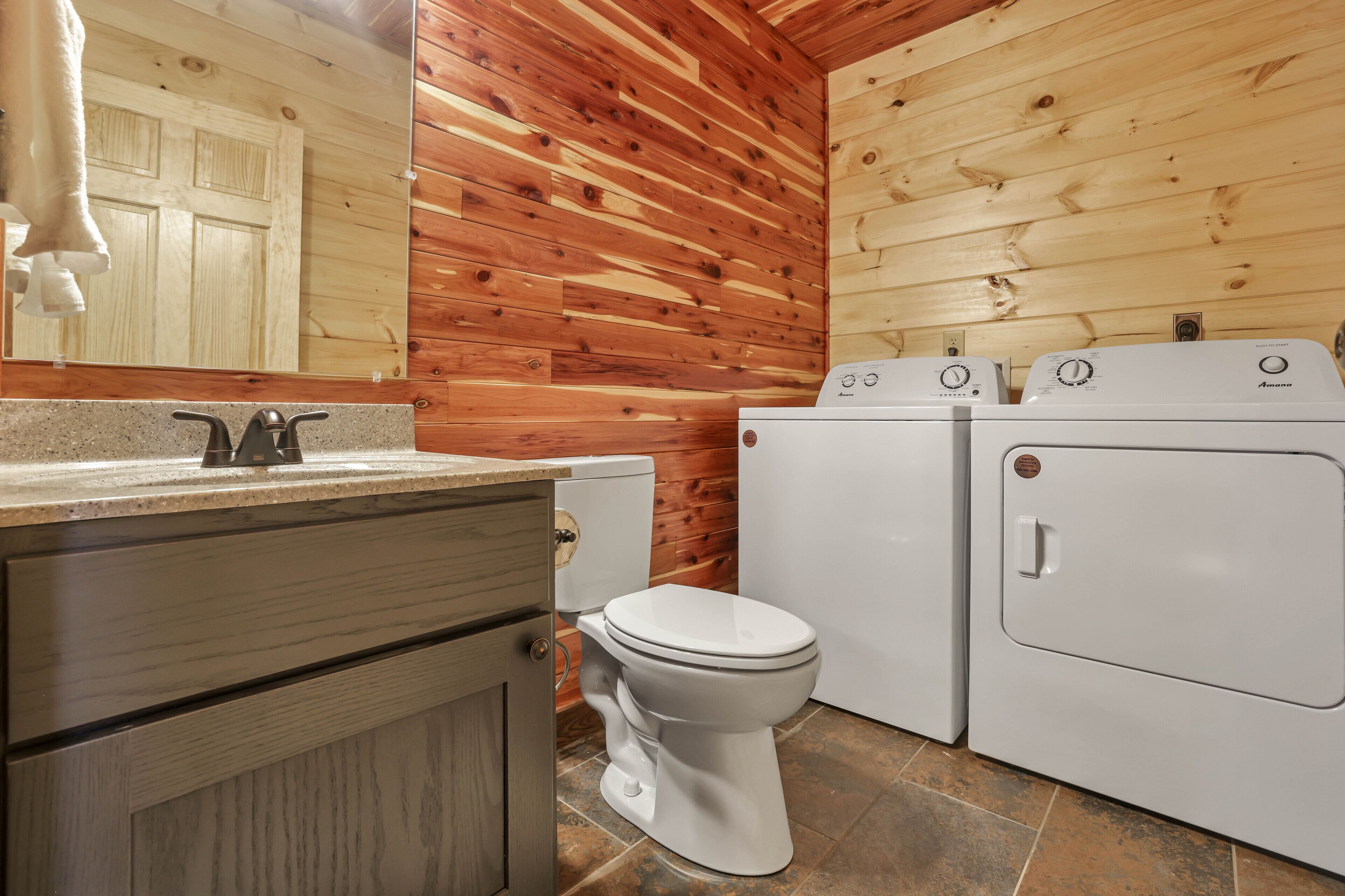 A bathroom with wooden walls, a toilet, and two washing machines.
