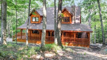 Une cabane en rondins avec un porche, entourée d’arbres.