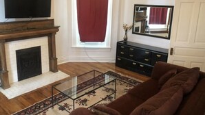 A living room with a fireplace, a television, a sofa, a mirror, and a window with curtains. - Cantrell’s on Broadway #1 (Nashville)