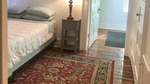 A bedroom with a bed, a nightstand, a lamp, a ceiling fan, and a red patterned rug. - Cantrell’s on Broadway #1 (Nashville)