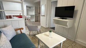A modern living room with a sofa, a coffee table, and a TV mounted on a wall. There are built-in shelves and a dining area in the background. - Spacious apartment 3 with balcony (Berchtesgaden)