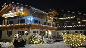 A two-story building with a balcony, snow-covered bushes, and illuminated decorations. - Spacious apartment 3 with balcony (Berchtesgaden)