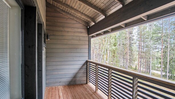 A wooden deck with a railing, a window, and a view of a forest.