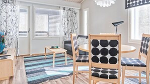 A modern living room with a wooden ceiling, a round table, two chairs with black and white patterns, a blue and black striped rug, and a white pendant light.