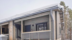 A modern log cabin with a covered porch and a metal railing.