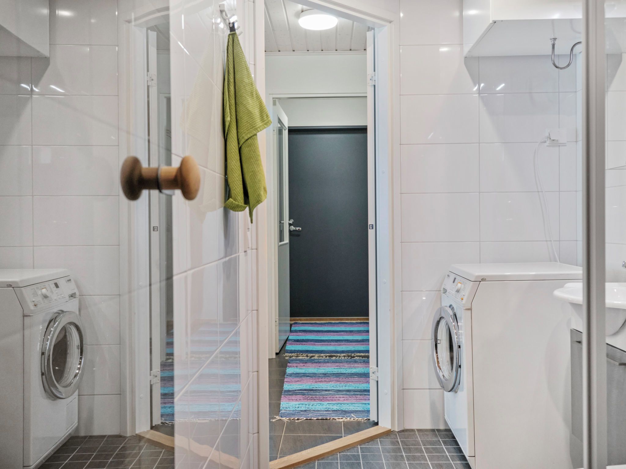 Et moderne badeværelse med en glasbrusekabine, en dør med et håndklæde hængende og to vaskemaskiner.