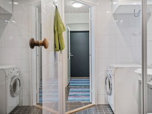 A modern bathroom with a glass shower enclosure, a door with a towel hanging, and two washing machines.