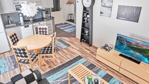 A modern apartment with a kitchen, dining area, and living room. It includes a dining table with chairs, a sofa, a coffee table, a TV, and a clock.