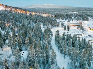 A snow-covered forest with a lodge and a ski lift in the background. - Luppokero 3 by Interhome (Pelkosenniemi)