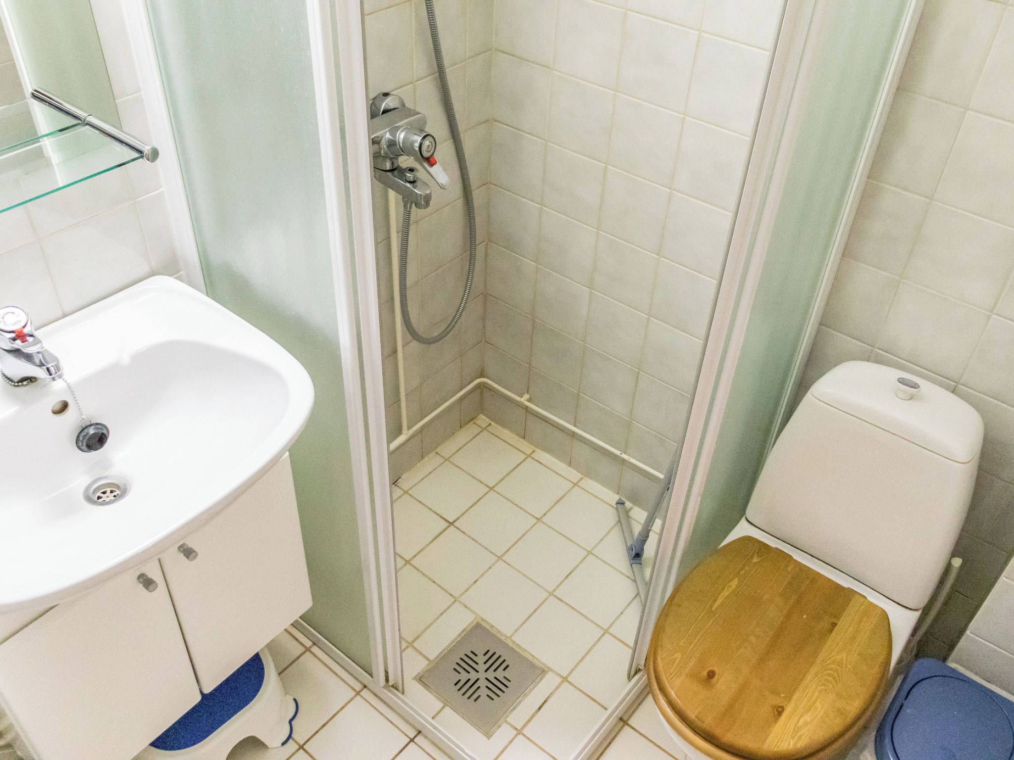 Un baño con lavamanos blanco, cabina de ducha y inodoro de madera.