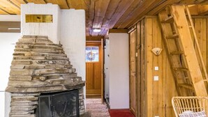 Una chimenea de piedra, paredes de madera, una silla de mimbre y una puerta de madera.