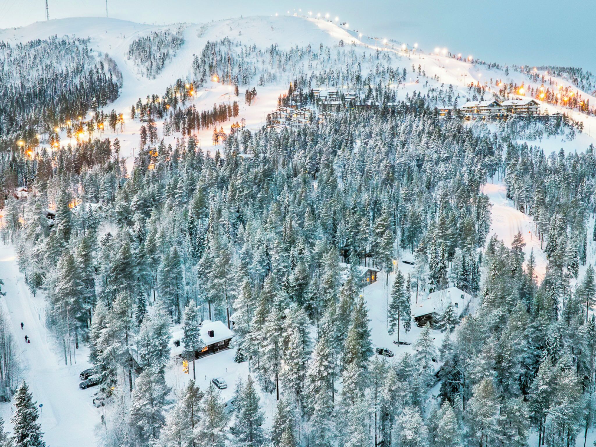 A snow-covered mountain resort with multiple buildings, ski slopes, and a dense forest.