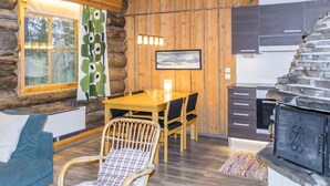 Interior de una cabaña de troncos con comedor, sofá, chimenea y cocina.