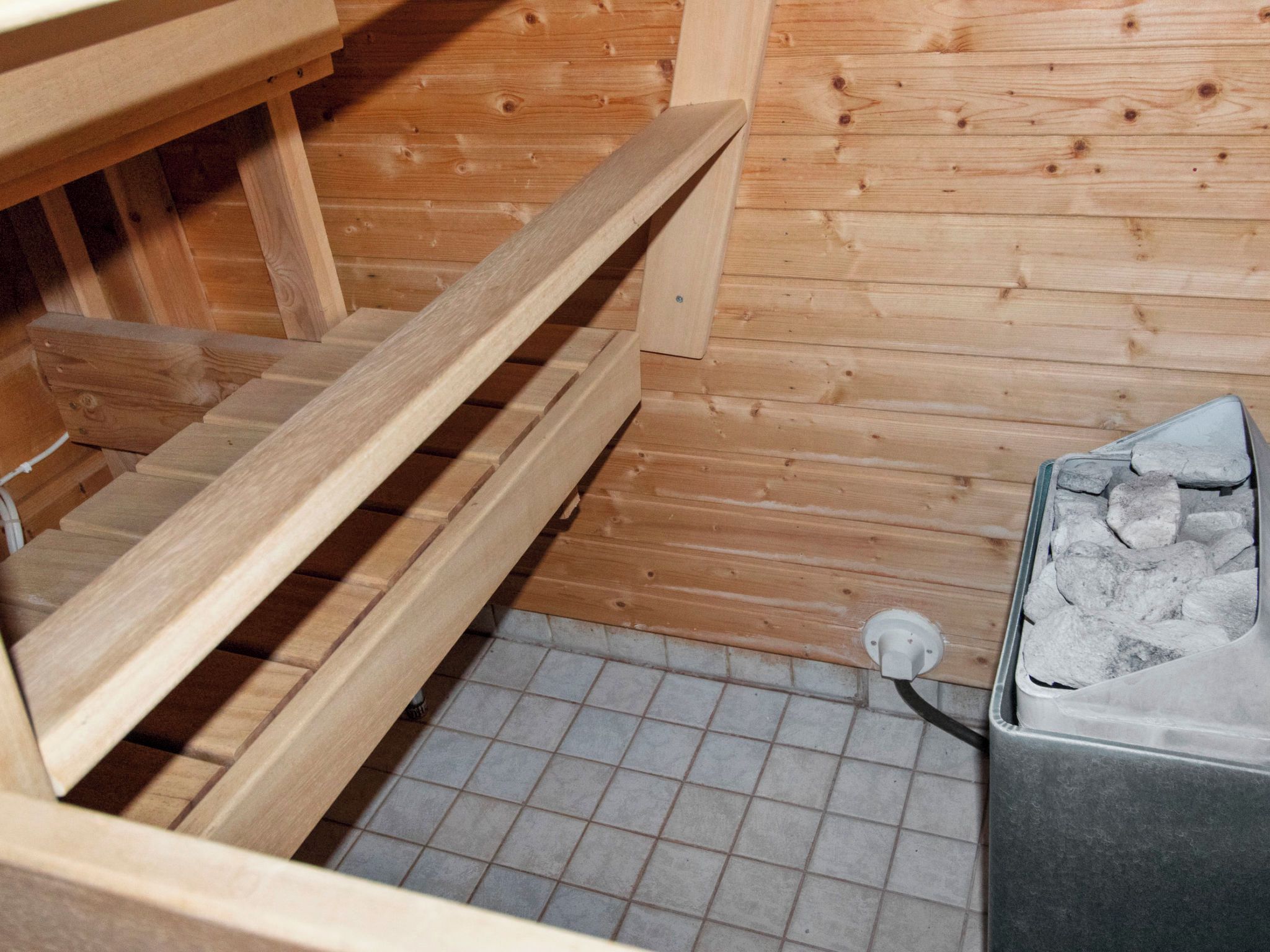 Un sauna avec des bancs en bois, un sol carrelé et un récipient en pierre.