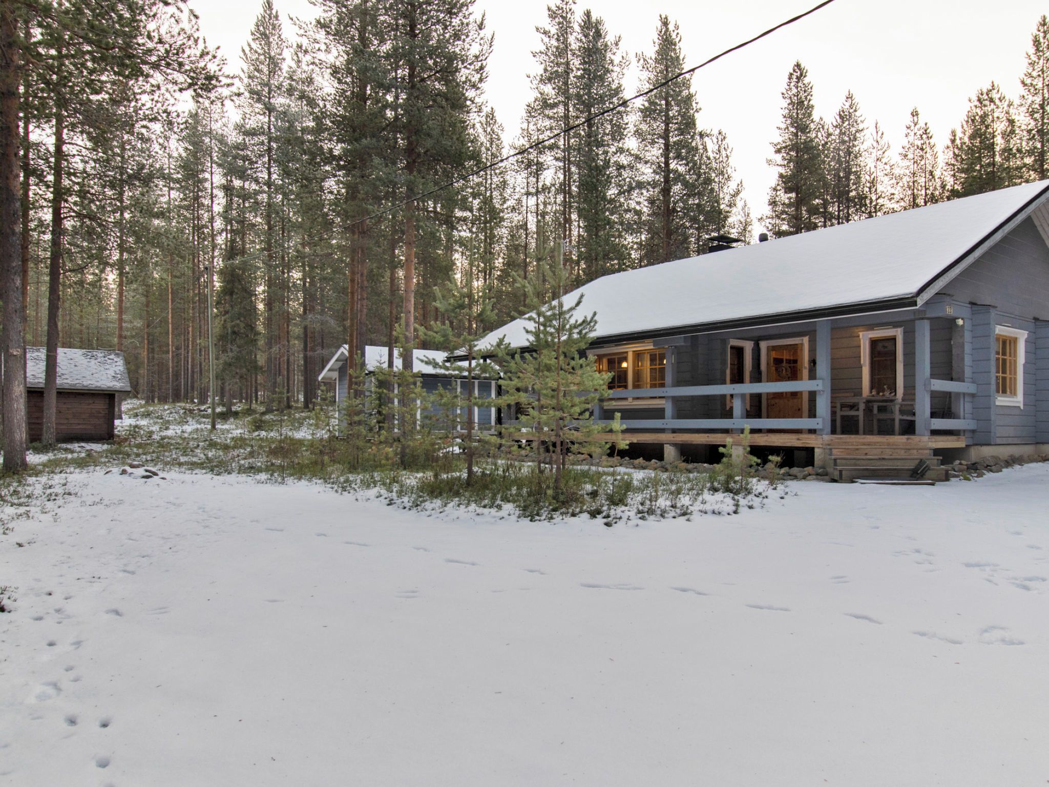 A cabin with a wooden deck, surrounded by a snowy landscape and tall pine trees.
