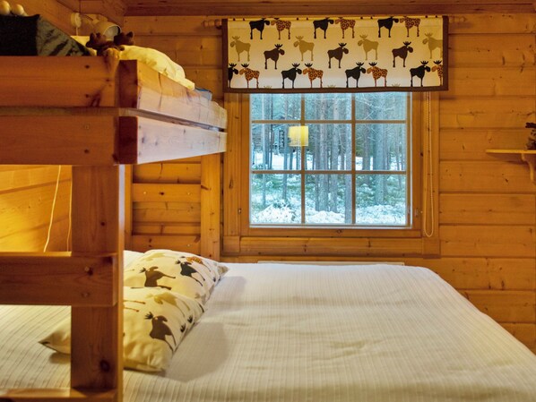 A cabin room with a bunk bed, a window with a view of a snowy forest, and a patterned curtain.