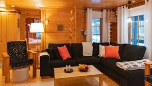 Um interior acolhedor de cabana de madeira, com um sofá preto, uma mesa de centro de madeira e uma cadeira.