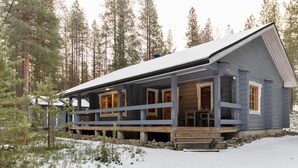 Uma cabana com deck de madeira, janelas amplas e telhado coberto de neve.
