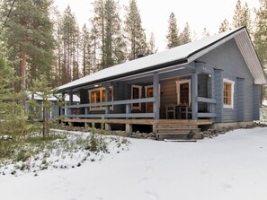 Une cabane dotée d’un porche, entourée de neige et d’arbres.