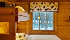 Um quarto de cabana aconchegante com beliche, janela com vista para uma floresta nevada e cortina estampada.