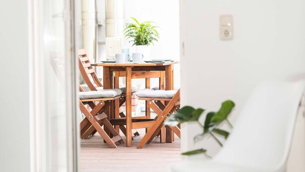 Una mesa de madera con cuatro sillas, una planta en maceta y una pared blanca.