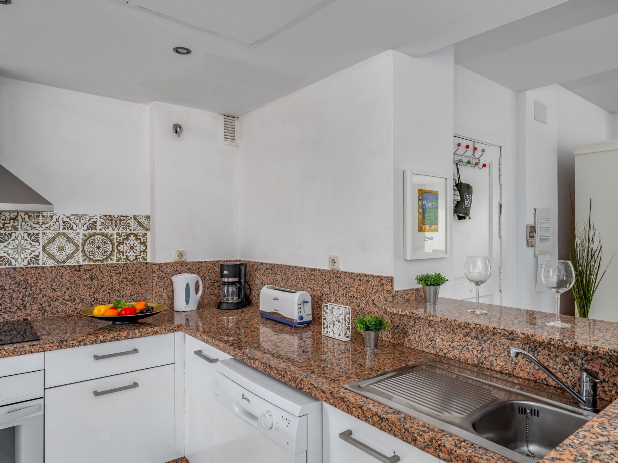 Eine moderne Küche mit Granit-Arbeitsplatten, weißen Schränken, einer Kaffeemaschine, einem Toaster und einem Spülbecken.