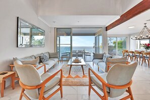 Un salon spacieux, doté d’un grand canapé, d’une table basse et offrant une vue sur la mer grâce à de grandes fenêtres.