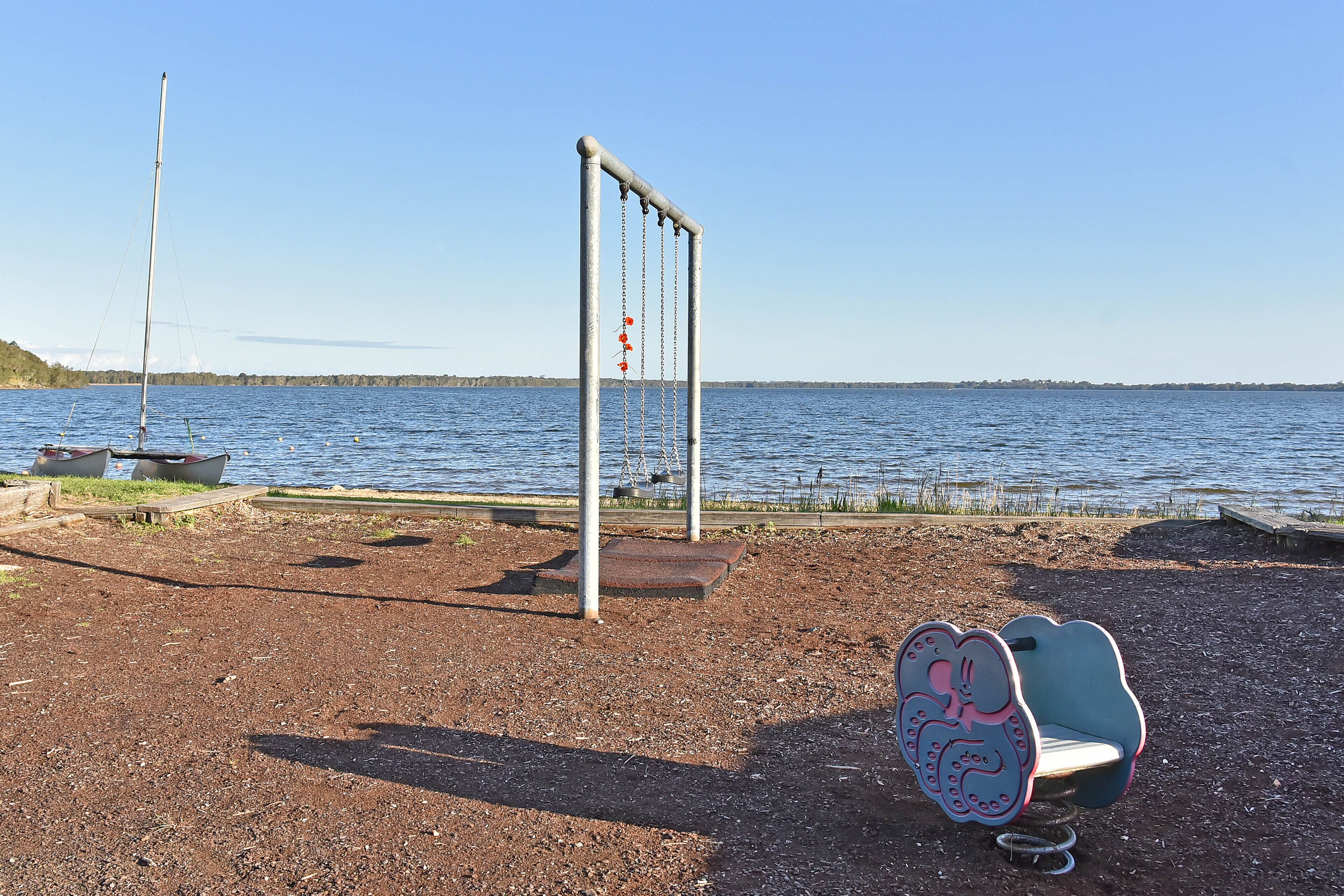 Ein Spielplatz mit Schaukel und Wippe am Seeufer.