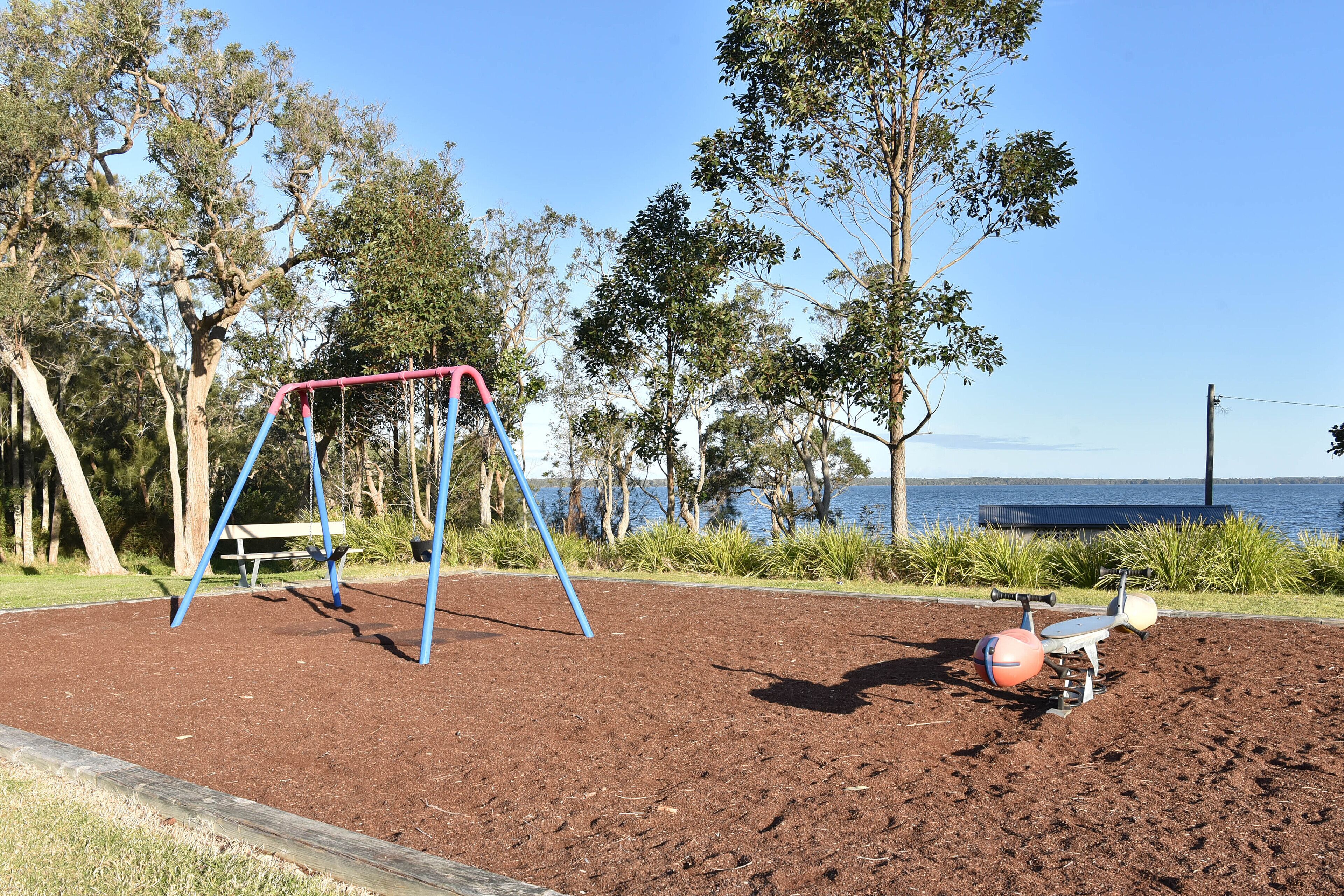 A playground with a swing set and exercise equipment near a body of water.