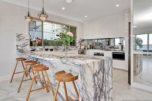 Une cuisine moderne dotée d’un îlot en marbre, de tabourets de bar et de luminaires suspendus.