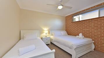 A bedroom with two single beds, a ceiling fan, a nightstand with a lamp, and a brick wall.