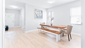 A dining area with a wooden table and benches, white walls, and a door in the background.