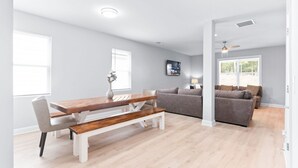 A modern living room with a wooden dining table, grey sofa, and a ceiling fan.