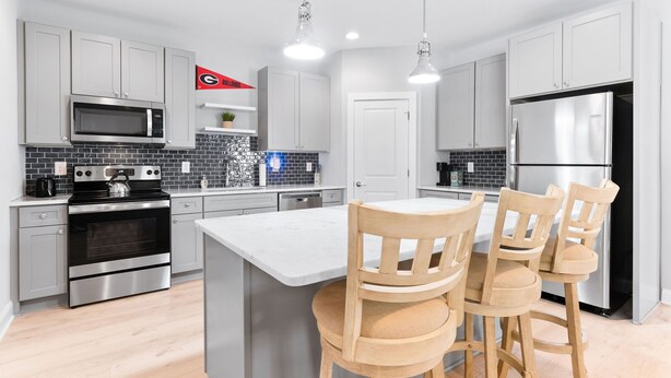 A modern kitchen with grey cabinets, a stainless steel refrigerator, a microwave, an oven, and a bar area with wooden chairs.