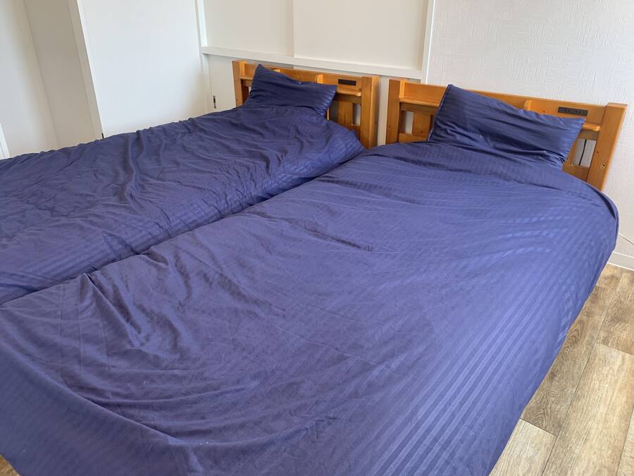 Cama de casal com cabeceira de madeira e colcha azul escura.