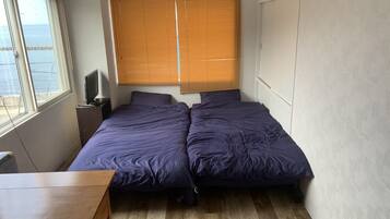 Une pièce avec un lit, une table et une fenêtre avec des stores.