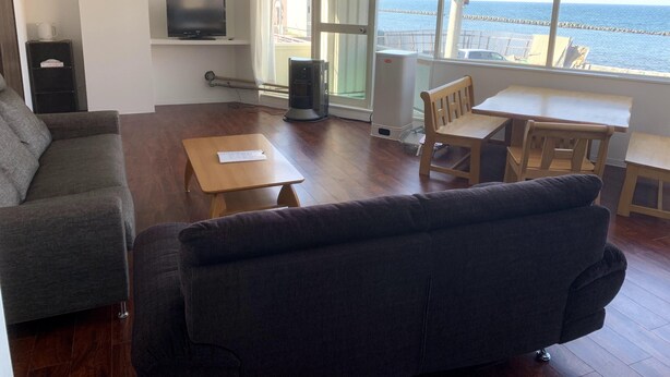 Una sala de estar con sofá, una mesita, televisor y vista al mar a través de amplios ventanales.