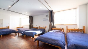 Habitación de hotel con cuatro camas individuales, cabeceros de madera, suelo de madera, una ventana con cortinas y un equipo de aire acondicionado en la pared.
