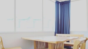 Una habitación con una mesa y sillas de madera, una ventana con cortinas azules y vistas a un edificio.
