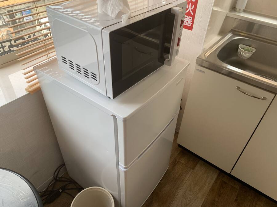 A compact kitchen with a microwave on top of a refrigerator, a sink with a dish rack, and a small countertop area.