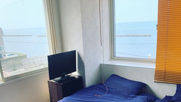 Een kamer met een bed, een televisie op een standaard en een raam met uitzicht op zee.