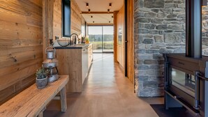 A modern kitchen with wooden walls, a stone accent wall, and a built-in stove. - Unique villa with fantastic views, near the beach (Callantsoog)