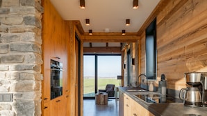 A modern kitchen with stone walls, wooden beams, and a large window overlooking a field. - Unique villa with fantastic views, near the beach (Callantsoog)